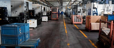 A wide view down the aisle of an industrial manufacturing facility lined with heavy machinery and storage crates.
