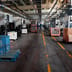 A wide view down the aisle of an industrial manufacturing facility lined with heavy machinery and storage crates.