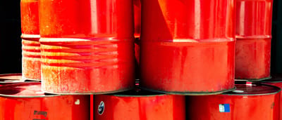 Bright red industrial oil barrels stacked tightly together in the daylight.