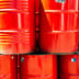 Bright red industrial oil barrels stacked tightly together in the daylight.