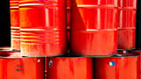 Bright red industrial oil barrels stacked tightly together in the daylight.