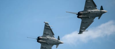 Two military fighter jets banking in formation against a blue sky.