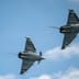 Two military fighter jets banking in formation against a blue sky.
