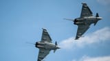 Two military fighter jets banking in formation against a blue sky.