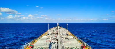 A view looking forward over the expansive deck of a large shipping tanker sailing across the open ocean under a bright blue sky.