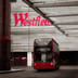 A red double-decker bus drives past the large red Westfield shopping center sign in London.