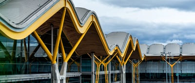 A modern airport terminal features a striking wavy roof supported by vibrant yellow architectural pillars.