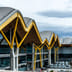 A modern airport terminal features a striking wavy roof supported by vibrant yellow architectural pillars.
