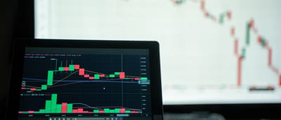 A laptop screen displays a dark-mode cryptocurrency trading chart with a series of red candlesticks indicating a steep market decline.