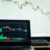 A laptop screen displays a dark-mode cryptocurrency trading chart with a series of red candlesticks indicating a steep market decline.