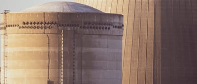 A close-up architectural view of a concrete nuclear reactor dome and cooling tower bathed in warm sunlight.
