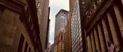 Looking up at the columned facade of the New York Stock Exchange and surrounding skyscrapers on Wall Street.