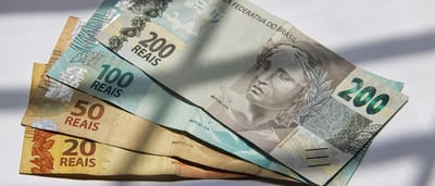 A selection of colorful Brazilian Real banknotes resting on a surface illuminated by dramatic striped sunlight.