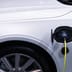 A white electric car is plugged in for charging, close-up view of the charging port.