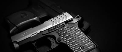 A black and silver pistol resting on a dark, shadowed surface.