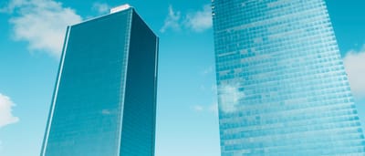 Two modern glass skyscrapers stand side by side against a bright blue sky.