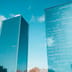 Two modern glass skyscrapers stand side by side against a bright blue sky.