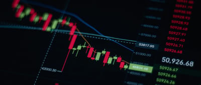 A close-up of a digital screen displaying a red, downward-trending candlestick stock market chart.