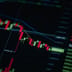 A close-up of a digital screen displaying a red, downward-trending candlestick stock market chart.