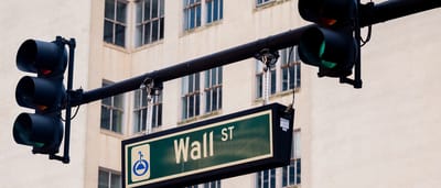 A street sign reading Wall St hanging next to a green traffic light in an urban setting.