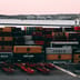 Stacks of cargo shipping containers fill a bustling industrial port at twilight.