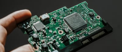 A close-up view of a person's hand holding a green semiconductor circuit board with microchips.