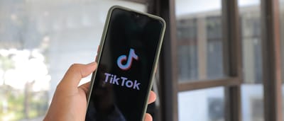 A person holding a smartphone displaying the TikTok logo on the screen.