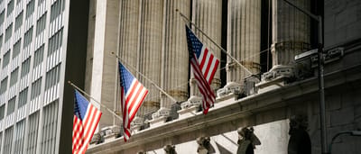 American flags hang between the grand stone columns of the New York Stock Exchange facade.