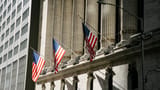 American flags hang between the grand stone columns of the New York Stock Exchange facade.