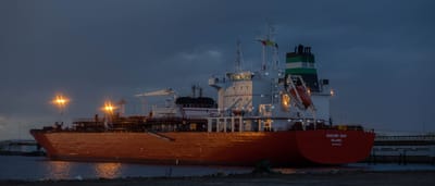 A large gas tanker ship illuminated at night while docked at an industrial port.
