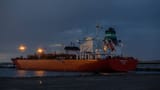 An illuminated industrial gas tanker ship docked at a port during twilight.