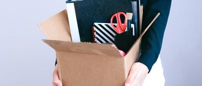 A professional holding a cardboard box packed with binders and office supplies.