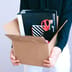A person holding a cardboard box filled with office supplies and binders.