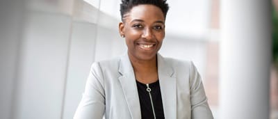A confident businesswoman smiles warmly in a bright, modern office space.