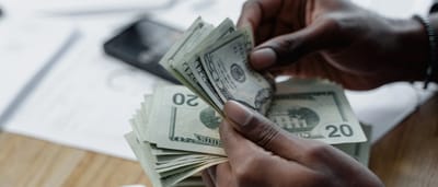Close-up of hands counting twenty-dollar bills over financial documents and a smartphone on a desk.
