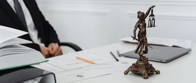 A small Lady Justice statue sits on a desk next to legal documents and an open laptop.