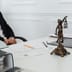A small Lady Justice statue sits on a desk next to legal documents and an open laptop.