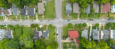 An aerial, top-down view of a classic suburban neighborhood intersection with houses, driveways, and green lawns.