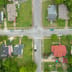 An aerial, top-down view of a classic suburban neighborhood intersection with houses, driveways, and green lawns.