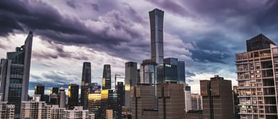Modern skyscrapers rise against a dark, stormy sky in Beijing's central business district.