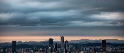 Heavy dark clouds hang over the modern skyline of Seoul at twilight.