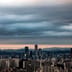 Heavy dark clouds hang over the modern skyline of Seoul at twilight.