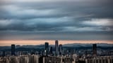 Heavy dark clouds hang over the modern skyline of Seoul at twilight.