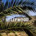 The iconic Hollywood sign on a sunny day in Los Angeles, California, framed by green palm leaves.