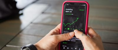 A person holds a smartphone displaying a green upward trend on a modern investing application.