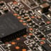 A macro view of a dark computer circuit board showcasing a microchip and intricate copper connections.