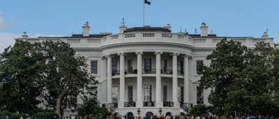 The South Portico of the White House on a clear day with the American flag flying above.