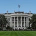 The South Portico of the White House on a clear day with the American flag flying above.