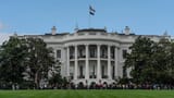 The South Portico of the White House on a clear day with the American flag flying above.