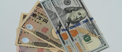 A close-up of a United States one-hundred-dollar bill resting on top of Japanese ten-thousand-yen banknotes.